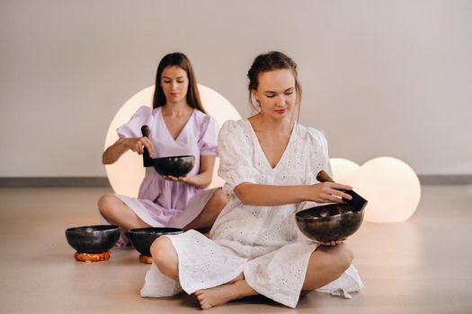 Two female yoga teachers playing a Tibetan bowl in the gym during a yoga retreat.