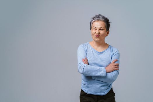 Showing positive dislike on her face mature business woman with grey hair in 50s, with hands folded and copy space on left for product placement isolated on white background.