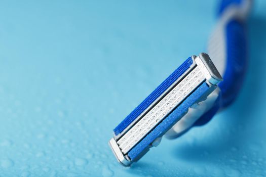 Blue shaving machine with sharp blades on the background of ice cubes close-up. The concept of cleanliness and frosty freshness