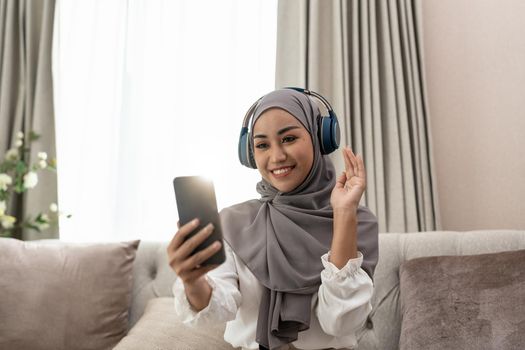 Muslim woman sitting on sofa and video conference calling on mobile phone. Muslim asian woman video call