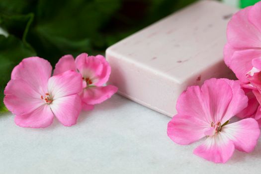 Pink bar of soap with bright pink geranium flowers.