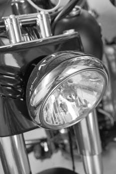 Closeup front view of a head light on a motorbike. A monochrome vintage motorcycle in black and white. One modern silver chrome transportation vehicle. Maintenance on a classic retro custom bike.