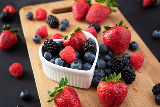 Fresh strawberries, blueberries and blackberries on a wooden cutting board