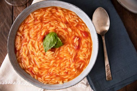 Bowl of orzo pasta and tomato soup with basil