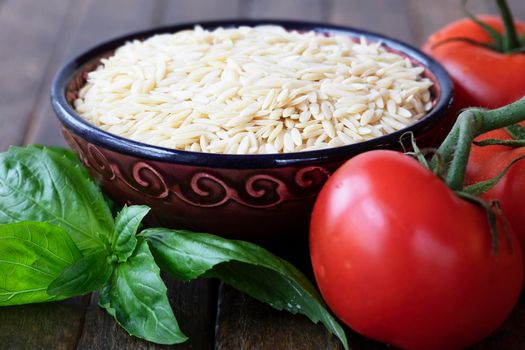 Dried orzo pasta in bowl with basil and tomato