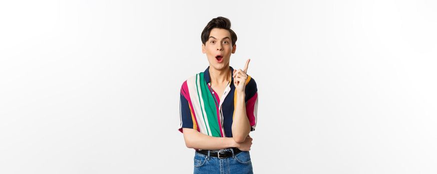 Portrait of young handsome guy having an idea, raising finger and saying suggestion, standing over white background.