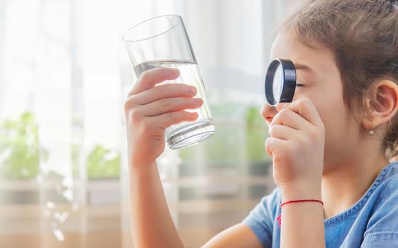 The child examines the water with a magnifying glass in a glass. Selective focus. Kid.