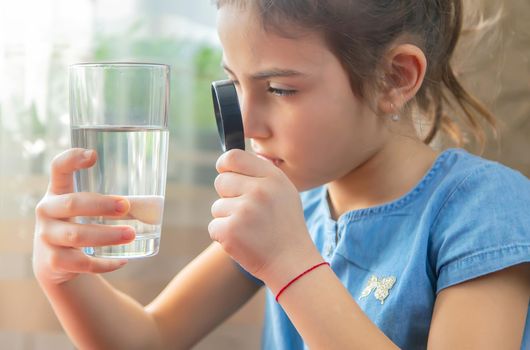 The child examines the water with a magnifying glass in a glass. Selective focus. Kid.