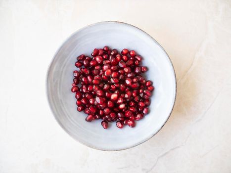 Fresh pomegranate seeds in bowl on marble surface, flat lay.
