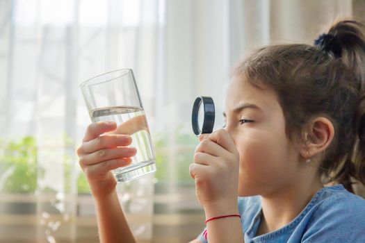 The child examines the water with a magnifying glass in a glass. Selective focus. Kid.