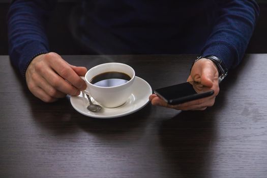 A man at a table with a phone and a cup of coffee. Selective focus. People.