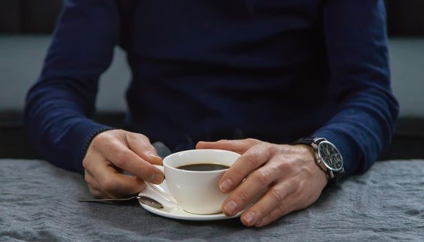 A man at the table with a cup of coffee. Selective focus. Drink.