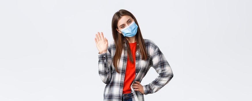 Different emotions, covid-19 pandemic, coronavirus self-quarantine and social distancing concept. Attractive coquettish young woman in medical mask, tilt head cute and waving hand, greet, say hello.