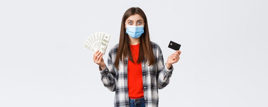 Money transfer, investment, covid-19 pandemic and working from home concept. Excited young woman earn or win lots of cash, showing dollars and credit card, wearing medical mask.