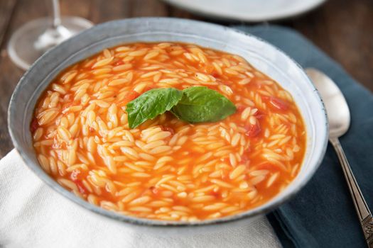 Bowl of orzo pasta and tomato soup with basil