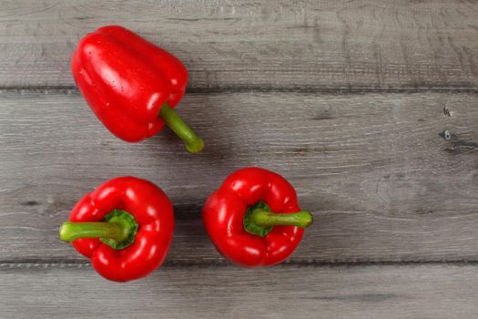 Tabletop view - three red bell peppers on gray wood desk.