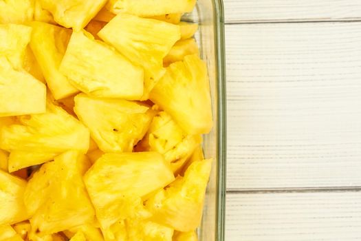 Tabletop view - close up of ripe pineapple cut into pieces, in glass bowl placed on white boards desk.