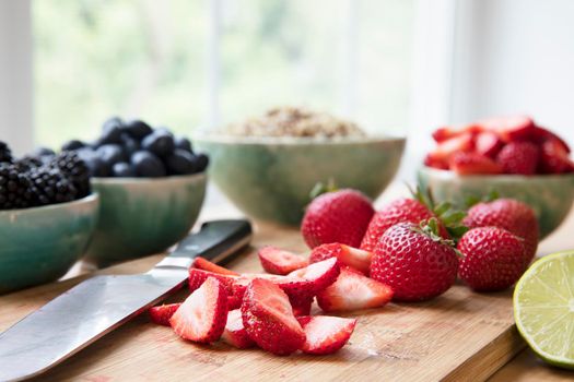 Sliced and whole strawberries on cutting board with knife, horizontal orientation.