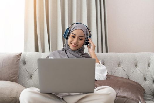 Asian muslim woman having video teleconference on her laptop at home, online learning or working from home concept.