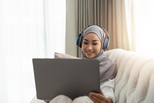 Asian muslim woman having video teleconference on her laptop at home, online learning or working from home concept.