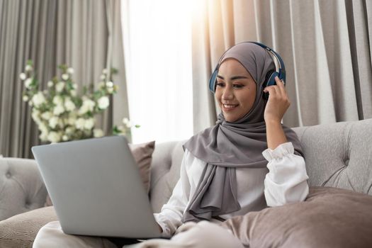 Asian muslim woman having video teleconference on her laptop at home, online learning or working from home concept.