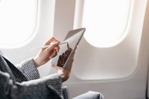 A successful asian businesswoman or female entrepreneur in formal suit in a plane sits in a business class's seat and uses a tablet computer during flight.