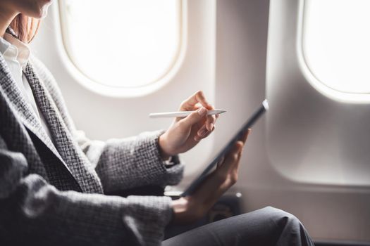 A successful asian businesswoman or female entrepreneur in formal suit in a plane sits in a business class's seat and uses a tablet computer during flight.