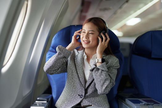 portrait of A successful asian business woman in a plane sits in a business class seat and uses a Around-Ears Headphones for playing music during flight. relax concept.