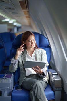 portrait of A successful asian businesswoman or female entrepreneur in formal suit in a plane sits in a business class's seat and uses a tablet computer during flight.