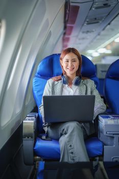 portrait of A successful asian business woman or female entrepreneur in formal suit in a plane sits in a business class seat and uses a computer laptop during flight.