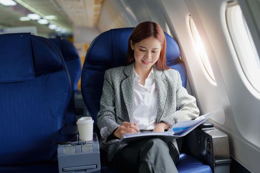 portrait of A successful asian business woman or female entrepreneur in formal suit in a plane sits in a business class seat and uses a pen with documents for work during flight.