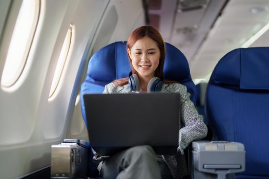 portrait of A successful asian business woman or female entrepreneur in formal suit in a plane sits in a business class seat and uses a computer laptop during flight.