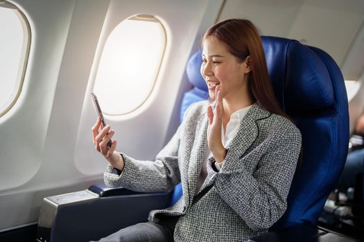 portrait of A successful asian businesswoman or female entrepreneur in formal suit in a plane sits in a business class's seat and uses a smartphone during flight.
