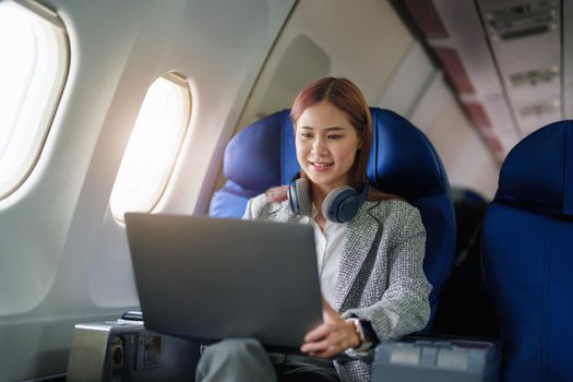 portrait of A successful asian business woman or female entrepreneur in formal suit in a plane sits in a business class seat and uses a computer laptop during flight.