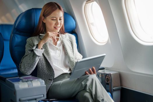 portrait of A successful asian businesswoman or female entrepreneur in formal suit in a plane sits in a business class's seat and uses a tablet computer during flight.