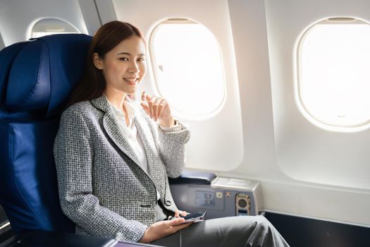 portrait of A successful asian businesswoman or female entrepreneur in formal suit in a plane sits in a business class's seat and uses a smartphone during flight.