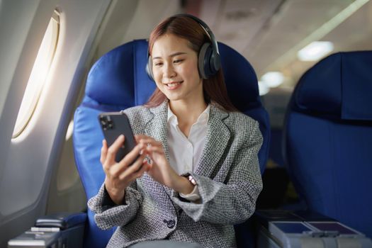 portrait of A successful asian business woman in a plane sits in a business class seat and uses a smartphone for playing music during flight, relex concept.