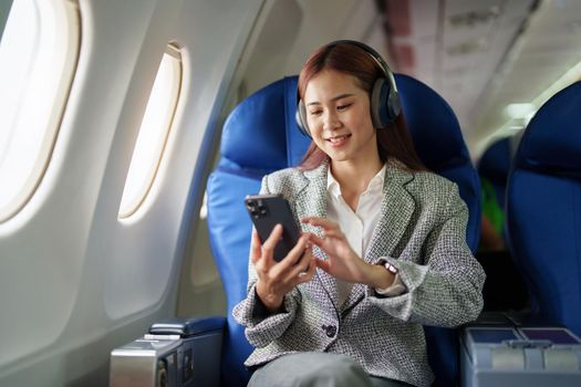 portrait of A successful asian business woman in a plane sits in a business class seat and uses a smartphone for playing music during flight, relex concept.