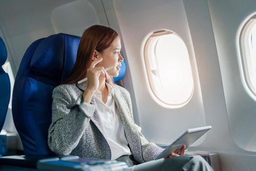 portrait of A successful asian businesswoman or female entrepreneur in formal suit in a plane sits in a business class's seat and uses a tablet computer during flight.