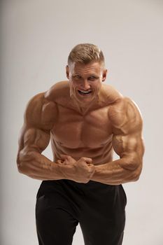 Athlete bodybuilder shows classic high power pose, bares his teeth. Good shape, bodybuilding lifestyle.