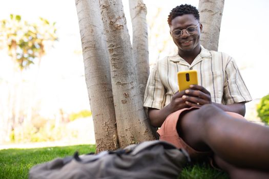 Black young man using mobile phone outdoors. Happy African american college student on campus sending text message with cell phone. Copy space. Education and technology concept.