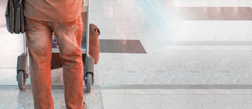 Banner of a fashionable young man in red jeans and shirt, with a trolley with luggage at the airport, back view, copy of the space on the right.