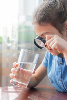 The child examines the water with a magnifying glass in a glass. Selective focus. Kid.