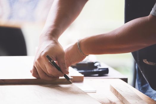 A carpenter measures the planks to assemble the parts, and build a wooden table for the customer