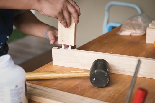 Woodworking operators are using glue to put together the wood parts to assemble and build a wooden table for their customers