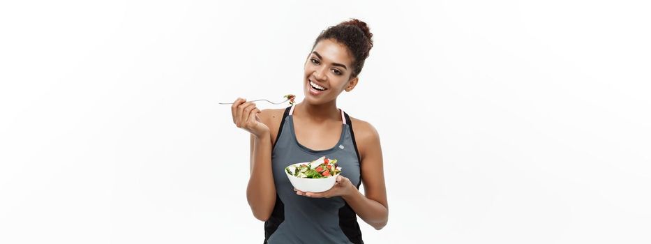 Healthy and Fitness concept - Beautiful American African lady in fitness clothes on diet eating fresh salad. Isolated on white background