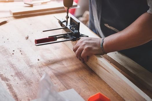 focus hand holding the wood handle, Woodworking operators are using a drill to drill holes in wood to assemble and build wooden tables for customers