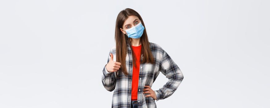 Coronavirus outbreak, leisure on quarantine, social distancing and emotions concept. Confident good-looking woman in medical mask give advice, recommend promo, show thumb-up in approval.