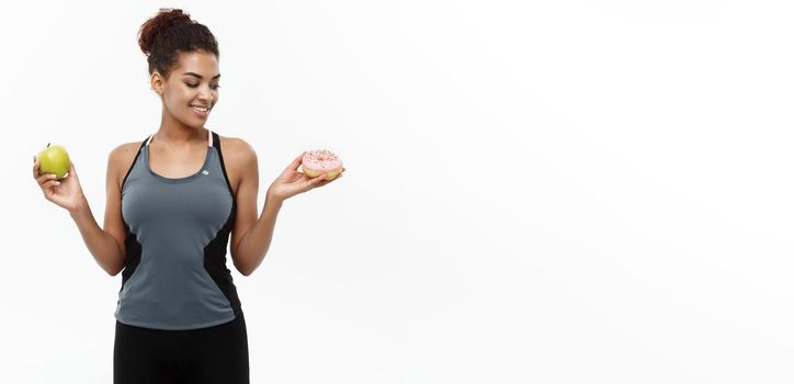 Healthy and diet concept - Beautiful sporty African American make a decision between donut and green apple. Isolated on white background