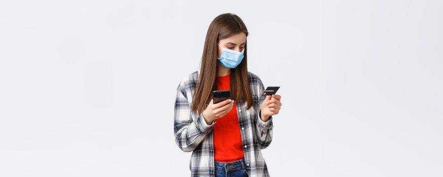 Coronavirus outbreak, working from home, online shopping and contactless payment concept. Girl in medical mask pay order groceries from grocery store to deliver, hold mobile phone and credit card.